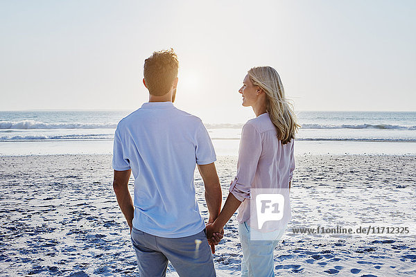 Paar hält sich am Strand bei Sonnenuntergang an den Händen.