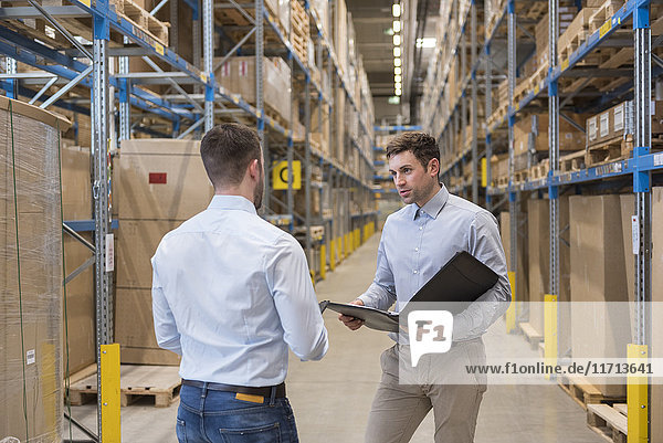 Two men with folder talking in factory warehouse