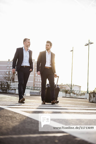 Two businessmen walking on parking place at sunset