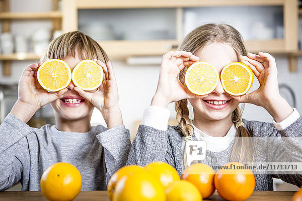 Bruder und Schwester bedecken ihre Augen mit Orangenscheiben.