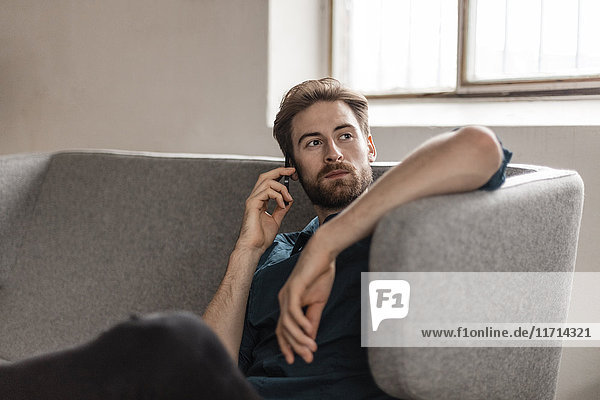 Porträt eines jungen Mannes am Telefon  der auf der Couch sitzt.