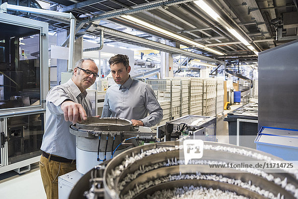 Two men in factory shop floor examining outcome of a machine