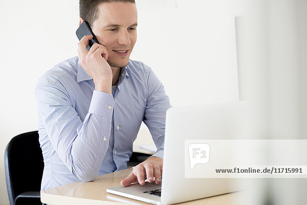 Smiling businessman on the phone using laptop