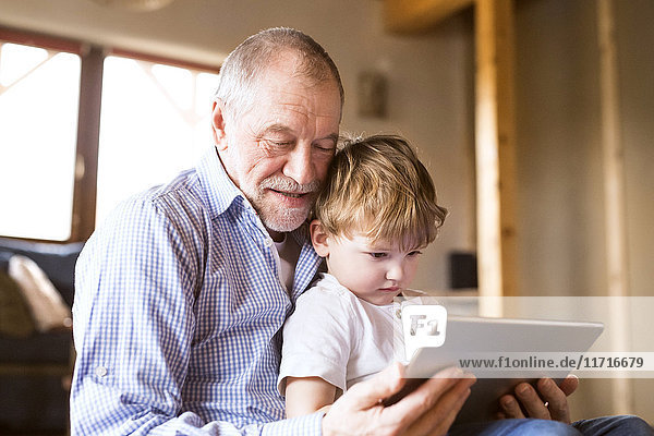 Grandfather and grandson sitting on floor  using digital tablet