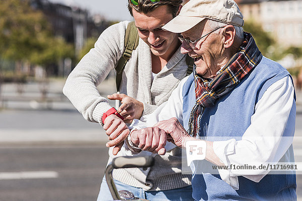 Glücklicher älterer Mann und erwachsener Enkel  der auf seine Armbanduhren schaut.