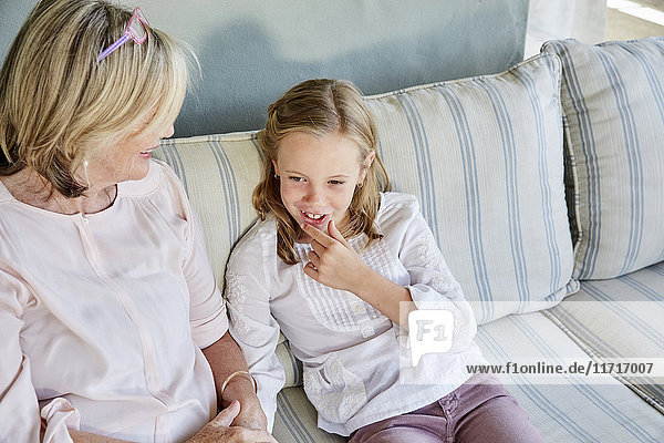 Lächelndes kleines Mädchen sitzt neben ihrer Großmutter auf der Couch.