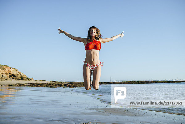 Smiling young woman jumping in the air on the beach