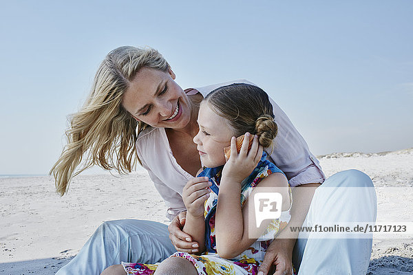 Glückliche Mutter und Tochter mit Muschel am Strand