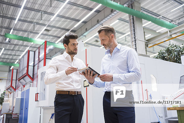 Two businessmen with tablet in factory shop floor discussing