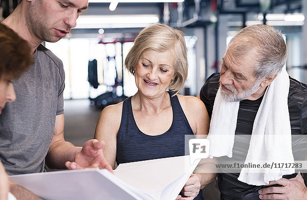 Group of fit seniors and personal trainer in gym looking in folder