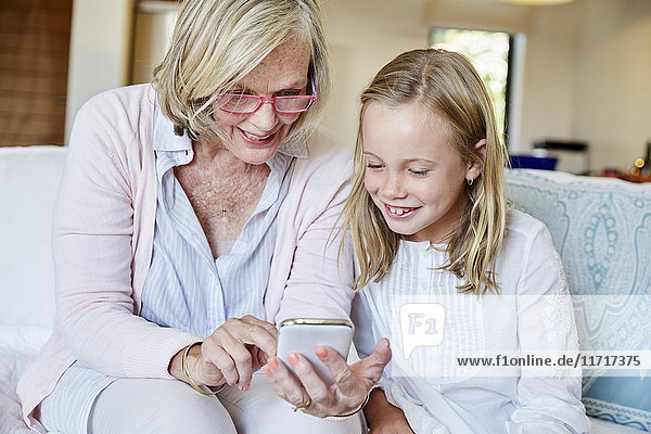 Grandmother and granddaughter sitting on the couch at home looking at smartphone