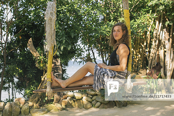 Junge Frau sitzt auf einer Schaukel in Strandnähe