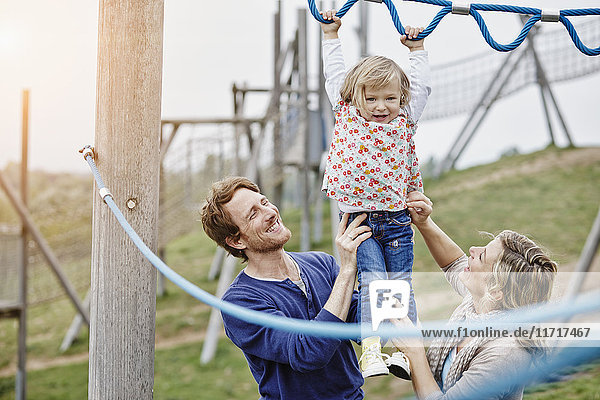 Girl on playground in climbing net supported by parents