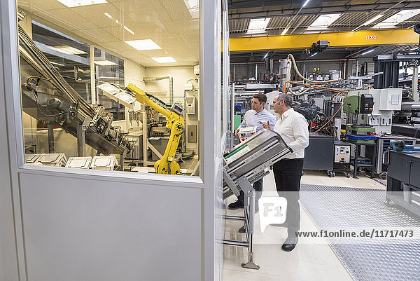 Two men talking in factory shop floor looking at industrial robot