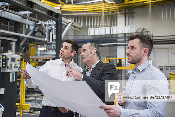 Three men with blueprint talking in factory shop floor