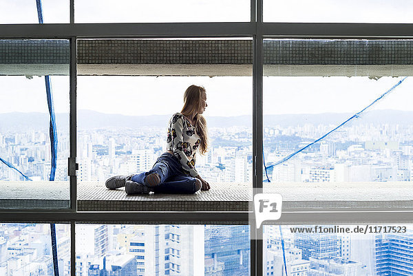 Young woman in high rise building sitting in window  looking over city