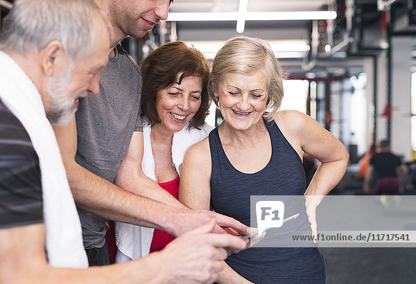 Gruppe von fit Senioren und Personal Trainer im Fitnessstudio mit Blick auf Tablette
