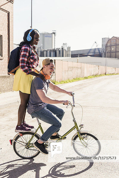 Young couple riding bicycle with girl standing on rack