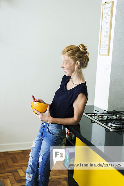 Ginger woman standing in kitchen eating breakfast
