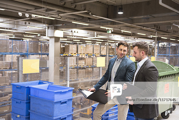 Two businessmen with documents talking in factory warehouse