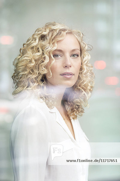 Portrait of blond businesswoman behind windowpane