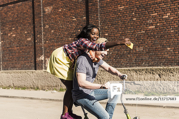 Young couple riding bicycle in the street  woman standing on rack  taking selfies