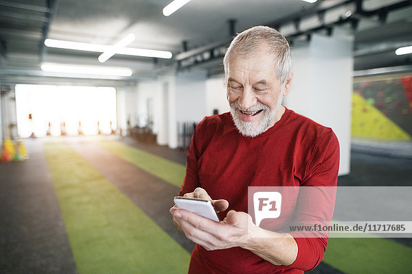 Fit senior man with smart phone in gym