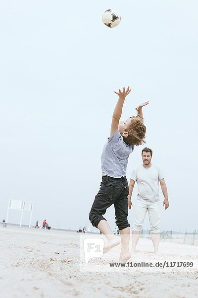 Vater und kleiner Sohn spielen mit dem Ball am Strand
