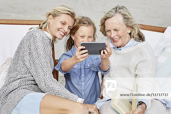 Mother  daughter and grandmother taking smartphone selfies on the beach