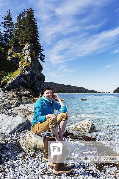 Frau sitzt auf Felsen am Ufer in der Nähe von Seldovia  Süd-Zentral-Alaska  USA