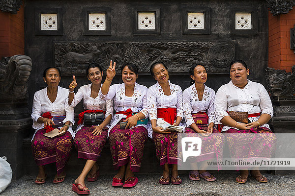 Eine Gruppe von Frauen  die in einer Reihe auf einer Bank sitzen und das gleiche Outfit tragen  in einem Hindu-Tempel; Insel Bali  Indonesien