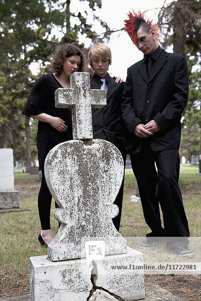 Drei Geschwister besuchen einen Grabstein auf einem Friedhof; Edmonton  Alberta  Kanada'.