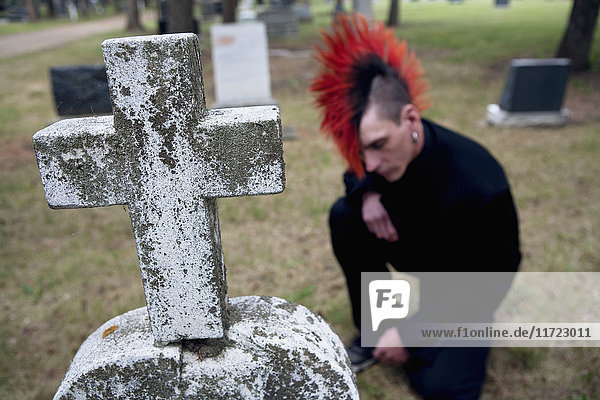 Ein junger Mann mit rotem Irokesenschnitt trauert um einen Grabstein auf einem Friedhof; Edmonton  Alberta  Kanada'.