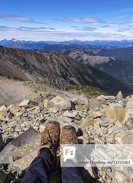Die Füße einer Frau stehen auf einem Felsen auf dem Gipfel des Mount Frosty mit Blick auf Windy Joe im E.C. Manning Provincial Park; British Columbia  Kanada.
