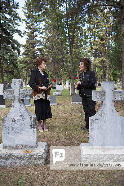 Zwei Frauen halten einzelne rote Rosen an einem Grab auf einem Friedhof; Edmonton  Alberta  Kanada'.
