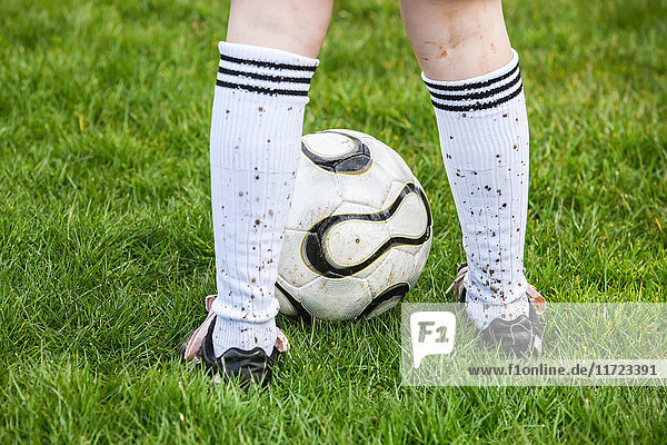 'A soccer player standing on a grass field with a soccer ball and mud splashed socks; Oregon  United States of America'