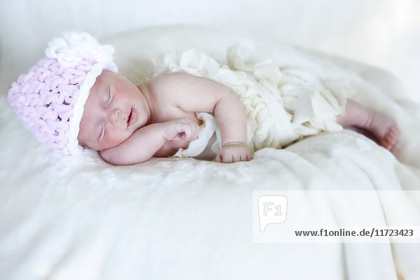 'A newborn baby lays sleeping on a white blanket wearing a pink knit hat; Washington  United States of America'