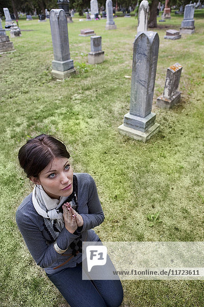 Eine junge Frau auf den Knien im Gebet auf einem Friedhof; Edmonton  Alberta  Kanada