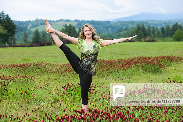 'A woman does yoga in a field of wildflowers with mountains in the background; Oregon  United States of America'