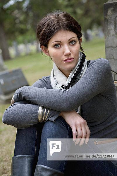 Eine junge Frau sitzt an einem Grabstein auf einem Friedhof; Edmonton  Alberta  Kanada