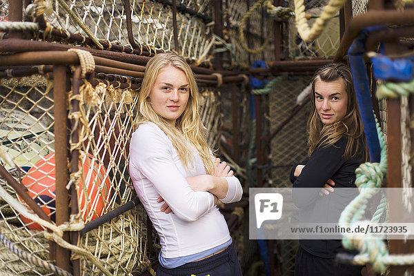 'Portrait Of Two Young Women In Front Of Commercial Crab Fishing Pots Stored In The Port Of King Cove  Alaska Peninsula; Southwest Alaska  United States Of America'