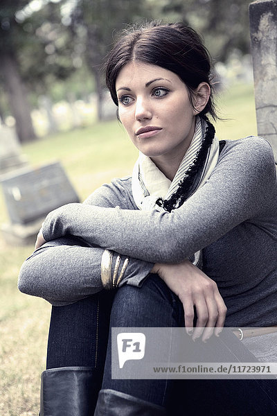 Eine junge Frau sitzt an einem Grabstein auf einem Friedhof; Edmonton  Alberta  Kanada .
