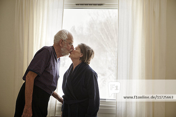 Älteres Paar küsst sich neben dem Fenster