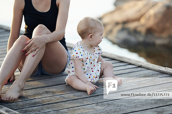Baby girl and woman sitting on pier