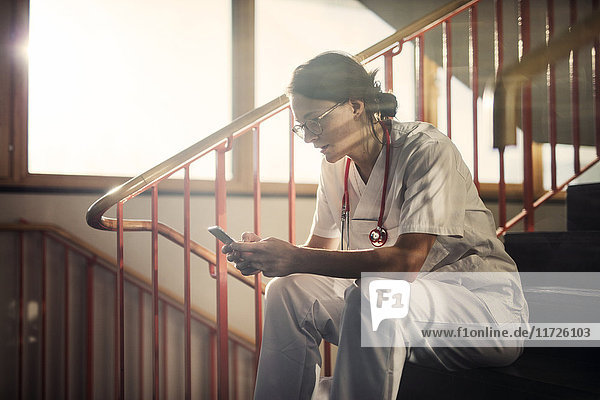Female doctor sitting on stairs with smartphone