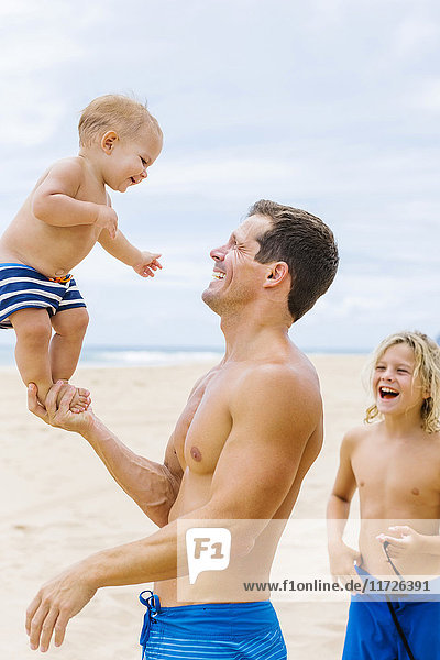 Vater spielt mit Söhnen (12-17 Monate  8-9) am Strand