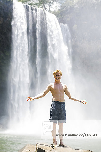 USA  Hawaii  Kauai  Junger Mann steht auf einem Felsen vor einem Wasserfall