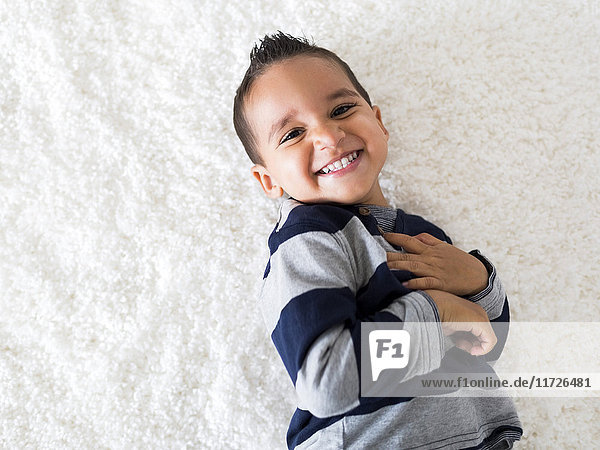 Boy (2-3) lying down on carpet and laughing