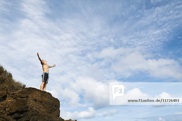Mann steht auf einem Felsen vor blauem Himmel