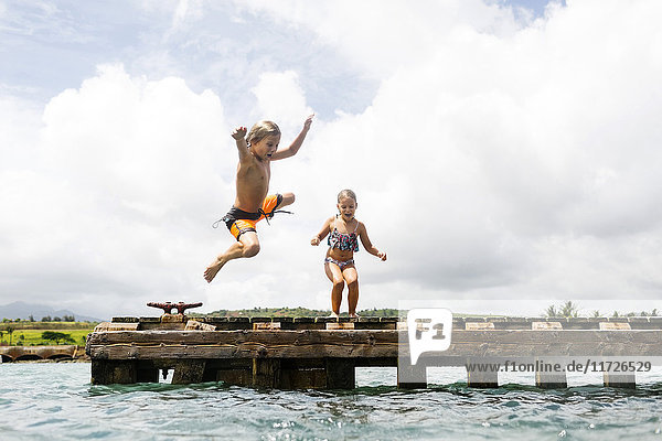 Boy (8-9) and girl (6-7) jumping into sea from jetty